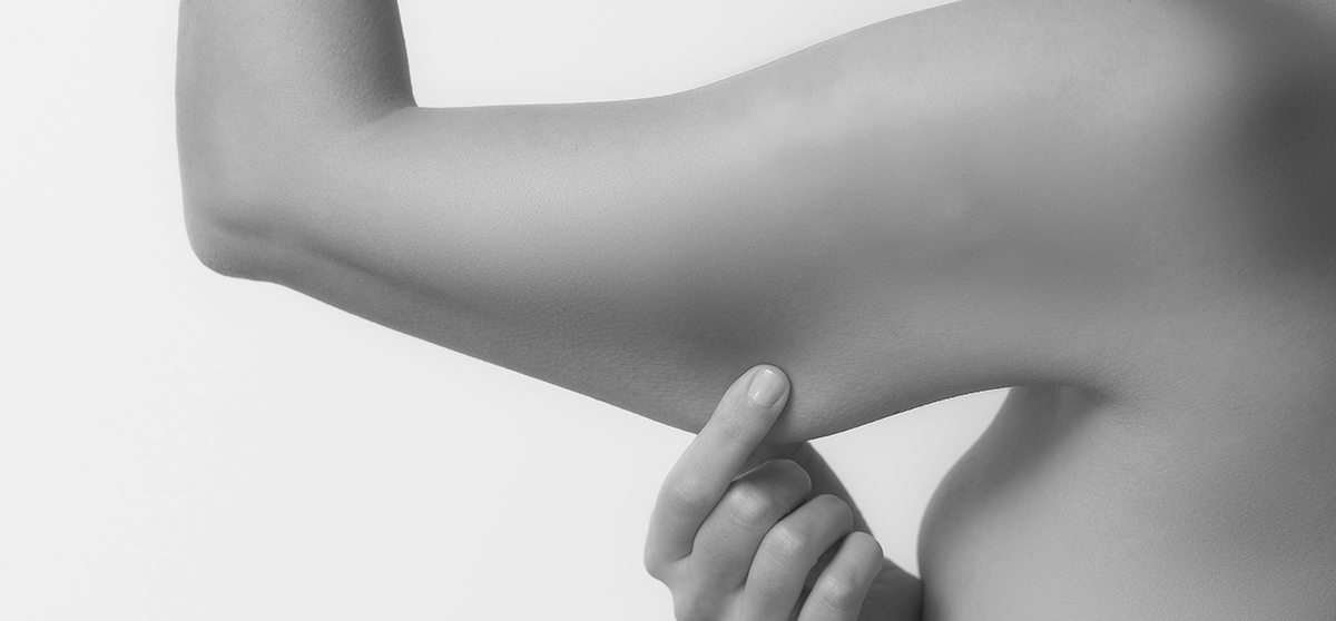 Woman testing the flabby muscle under her arm pulling it down with her hand as she checks for muscle tone or weight gain